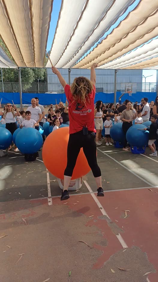 רינת קופצת מעל כדור כתום ענק מול קהל ילדים והורים